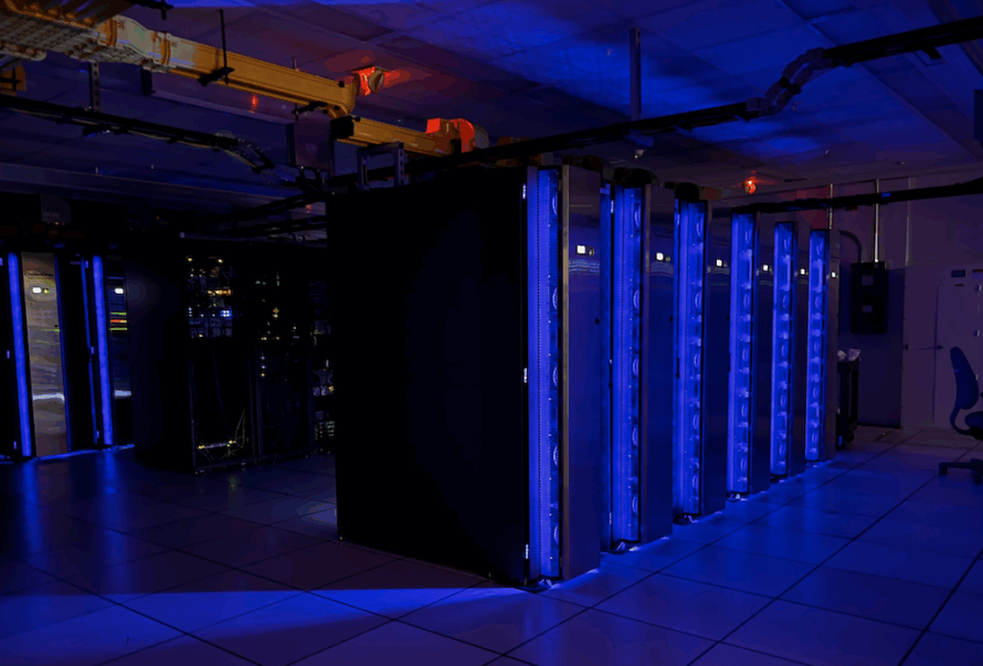 Computer cluster of several nodes highlighted by blue lights in an otherwise dark room.
